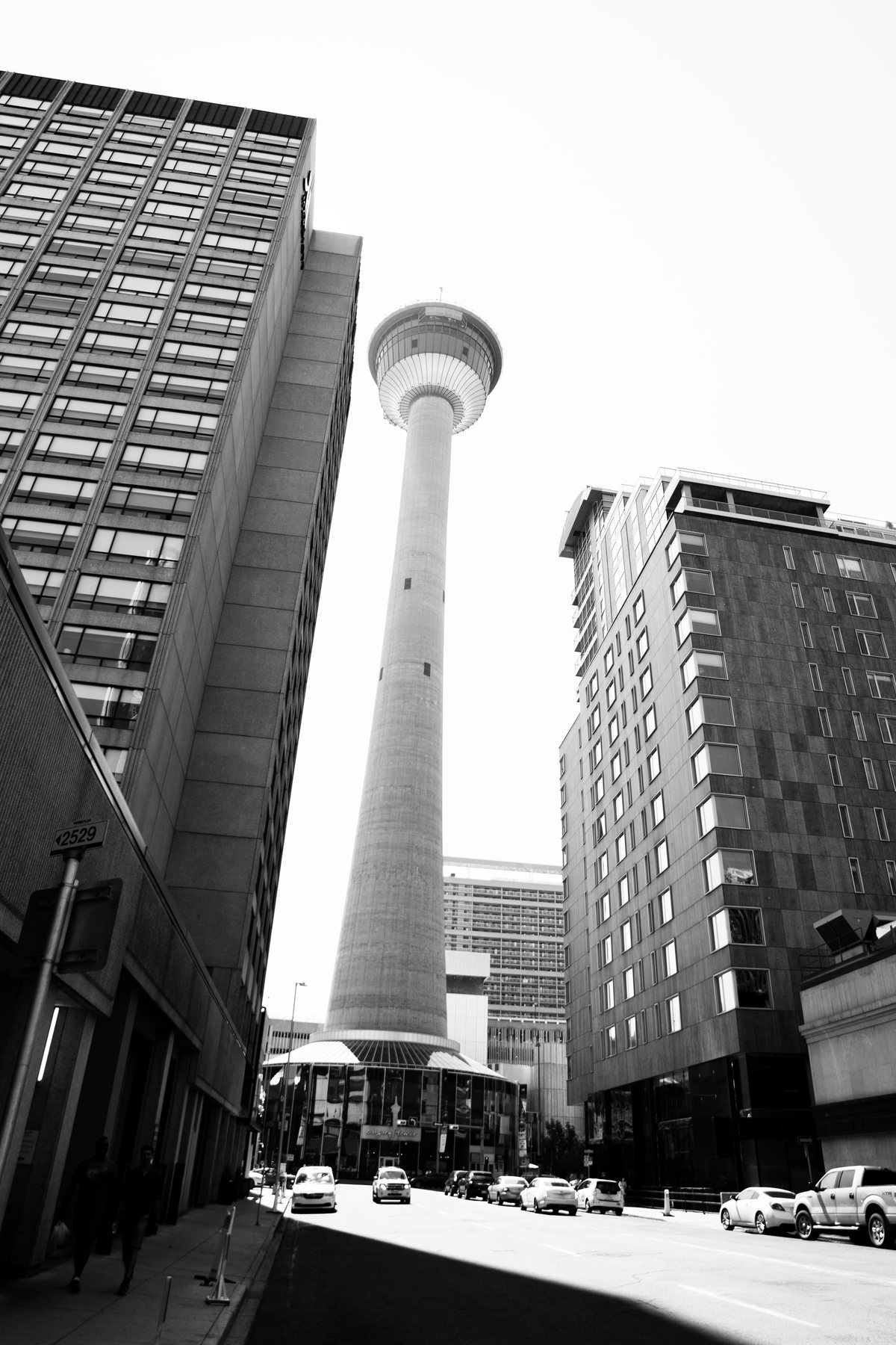 Black-and-white street view looking up at the Calgary Tower between downtown buildings